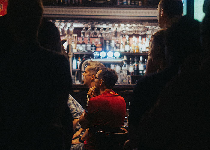 People watching a live event in a dimly lit bar, capturing moments of instant karma manifestations.