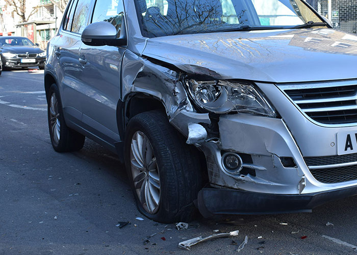 Silver SUV with front right side damage parked on city street illustrating instant karma manifestations in vehicle accidents.