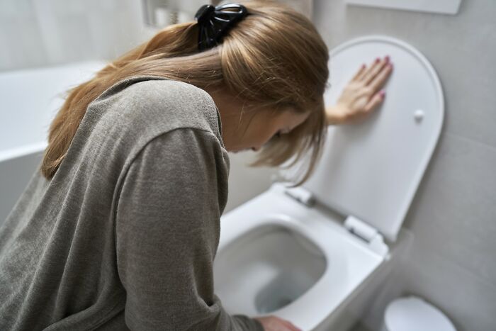 Woman leaning over toilet, experiencing drunk fumbles and bad decisions in a bathroom setting.