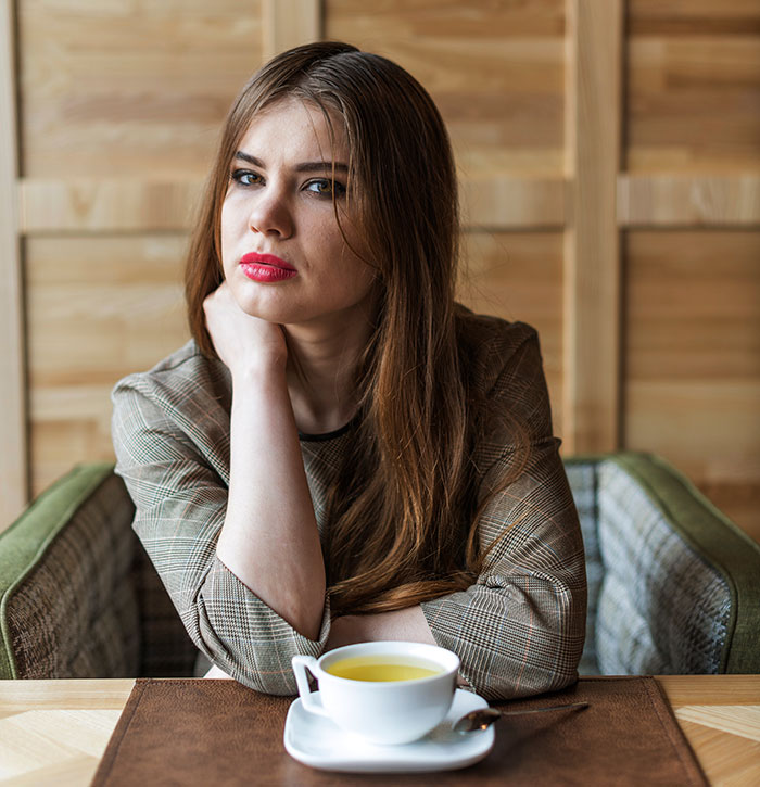 Woman sitting at a table with a cup of tea, looking thoughtful about a bill splitting and fat-shaming situation.