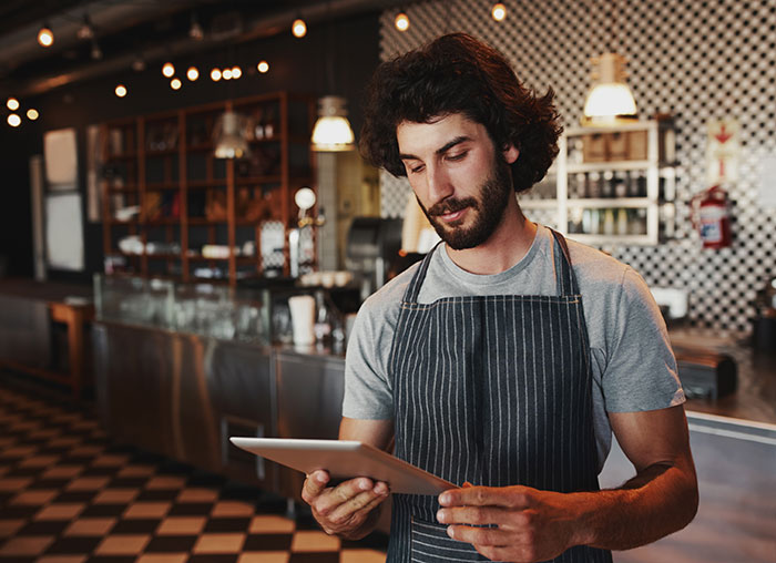 Man in apron in a modern restaurant reviewing a bill splitting situation on a digital tablet.