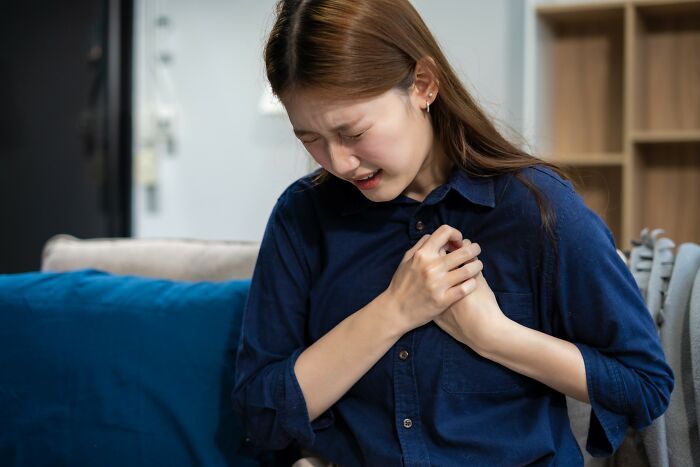 Young woman clutching chest in pain at home depicting medical problems far worse than people think