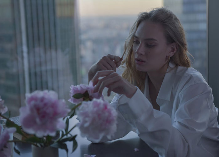 Woman in white shirt sitting by a window, looking distraught while touching pink flowers, reflecting on a difficult relationship truth.