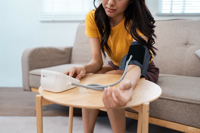 Young woman in yellow shirt checking blood pressure at home highlighting medical problems severity
