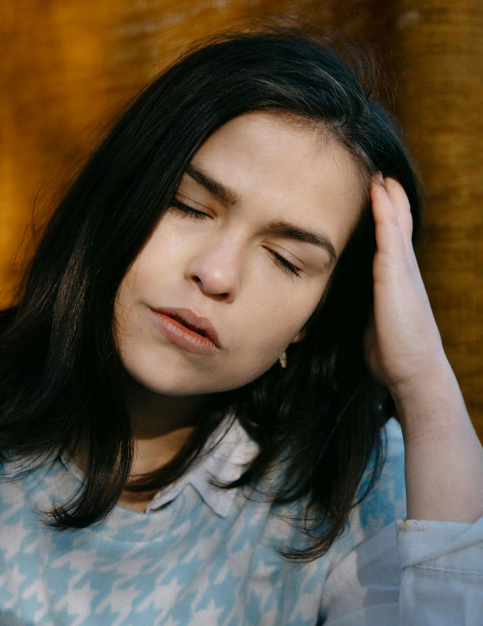 Stressed woman with closed eyes holding head, representing parents guilt-tripping daughter-in-law over babysitting.