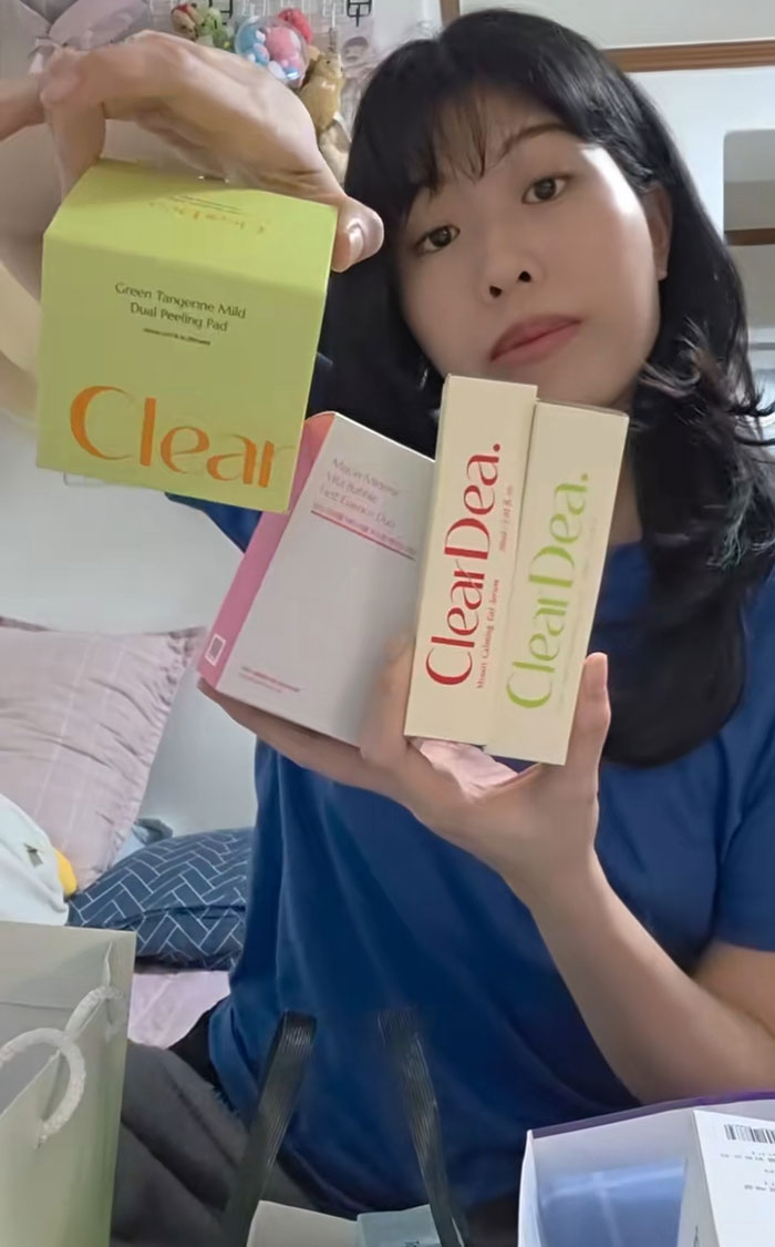 Woman showing skincare and beauty gifts received during job interviews in Korea, seated indoors in casual clothing.