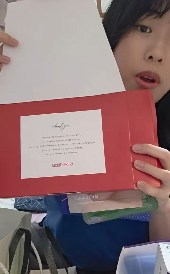 Woman showing gifts received while interviewing for jobs in Korea, featuring skincare and beauty products in a red box.