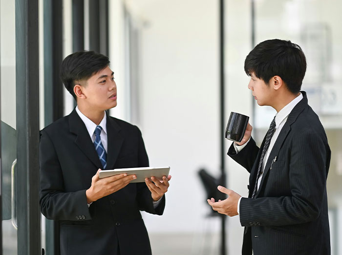 Two men in suits talking during a job interview in Korea, one holding a tablet and the other a coffee mug.