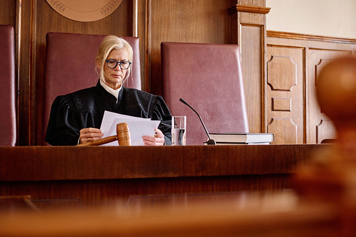 Female judge in black robe reviewing documents in courtroom, symbolizing legal battles and financial ruin conflict.