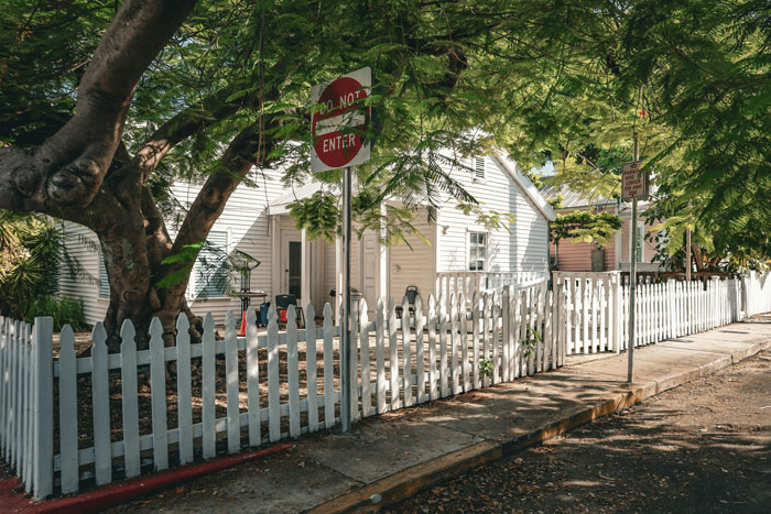 White picket fence surrounding a yard with trees and a house, illustrating new homeowners enjoying their fenced pool area.