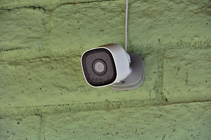 Security camera mounted on a green wall monitoring new homeowners enjoying their yard and pool in a fenced area.