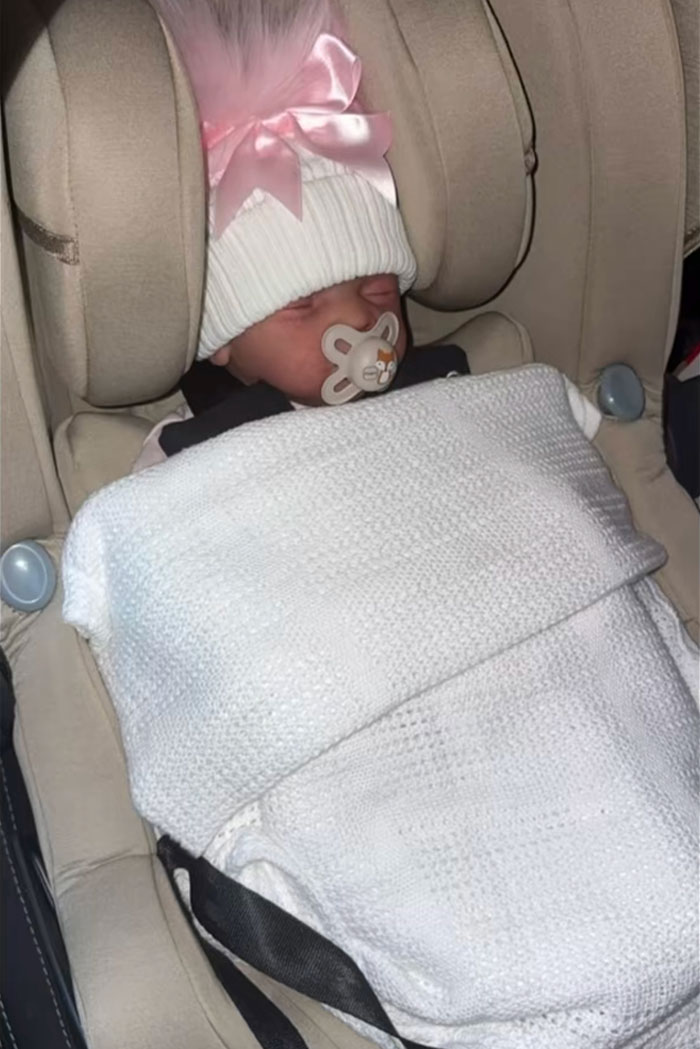 Baby doll wrapped in white blanket with pink hat in a car seat, linked to woman's outrageous 10-month lie story.