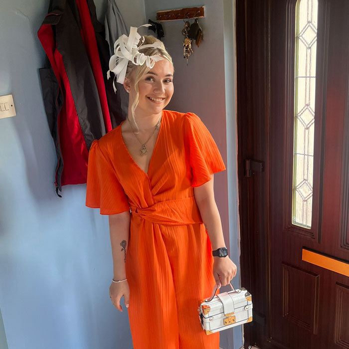Woman in orange dress smiling indoors near a door, related to story about woman&rsquo;s outrageous baby doll lie unraveling.