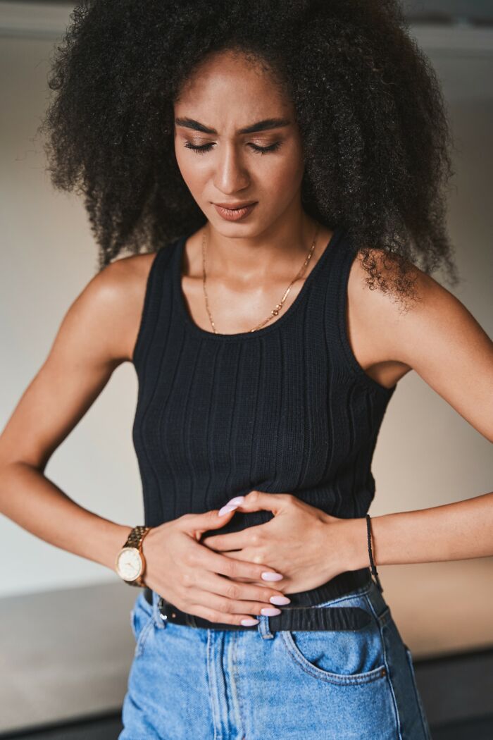 Young woman in a black tank top holding her stomach in pain, illustrating common medical problems unseen by many.
