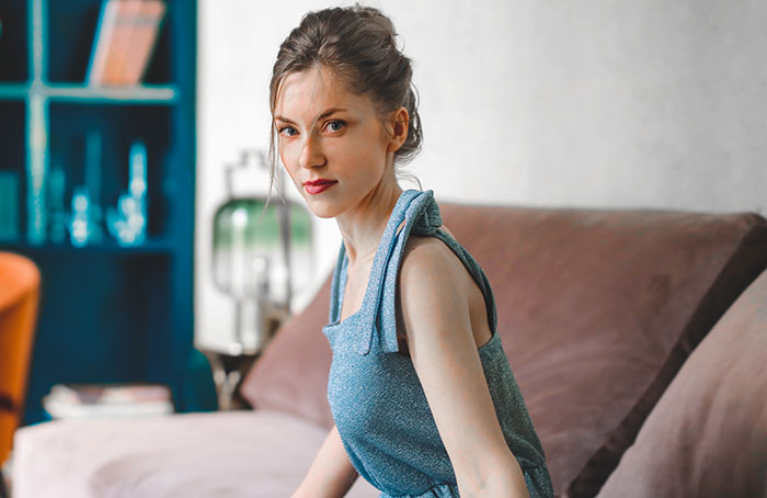 Young babysitter in a blue dress sitting on a couch, reflecting on weird and awkward babysitting moments.