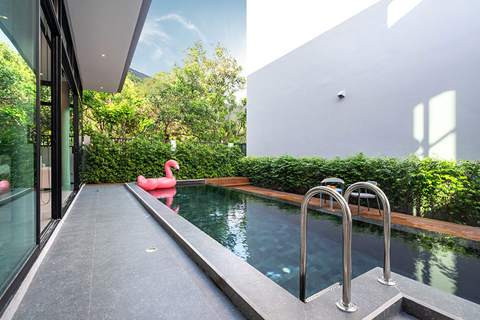 Modern backyard pool with a flamingo float, glass doors, and green plants, perfect for babysitters' weird and awkward moments.