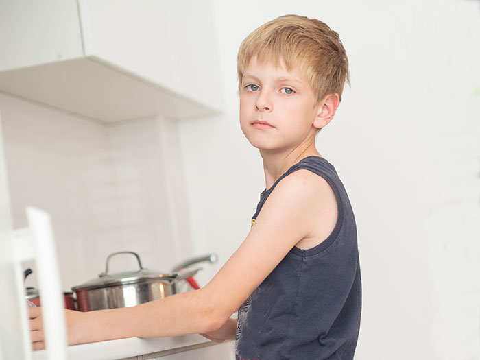 Young boy standing in kitchen with serious expression, illustrating babysitter awkward moments and weird experiences.