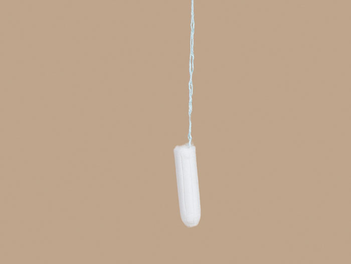 A white tampon hanging by its string against a neutral background, symbolizing awkward moments shared by babysitters.