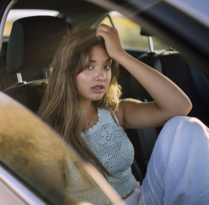 Young babysitter looking stressed and awkward sitting in a car reflecting weird babysitting moments and pay complaints