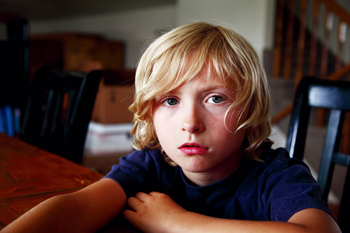 Young blond boy sitting at a table indoors, illustrating a babysitter’s awkward moments experience and babysitting challenges.