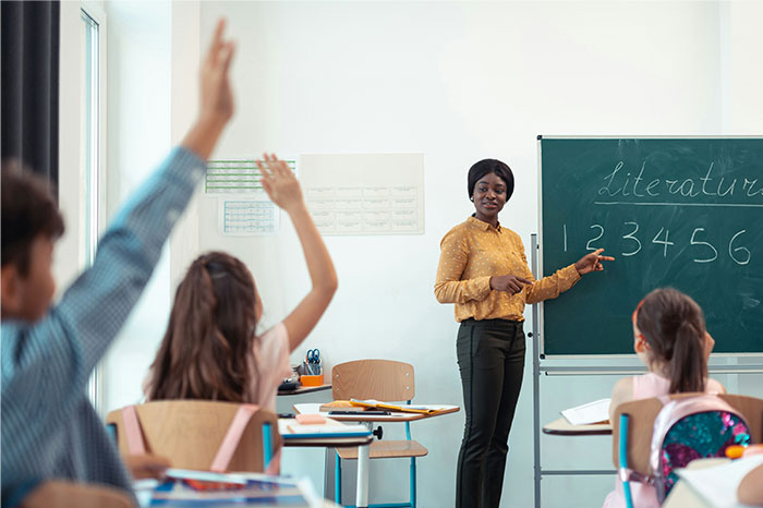 Teacher pointing at chalkboard numbers while students eagerly raise hands in a classroom illustrating work failure moments.