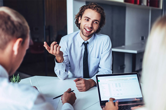 Young professional discussing work while colleagues use laptop and take notes during a casual office meeting showing work failure risks