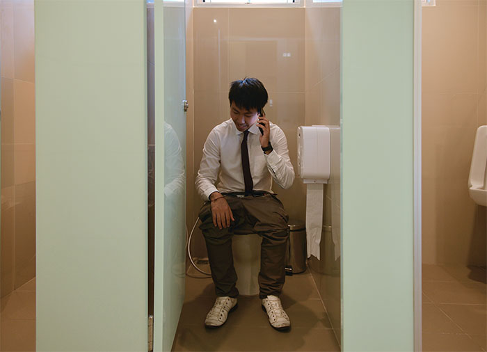 Man in office attire making a phone call while sitting on toilet, illustrating people failed spectacularly at work moments