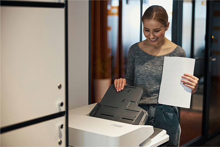 Woman smiling while using a printer showing a moment from people who failed spectacularly at work.