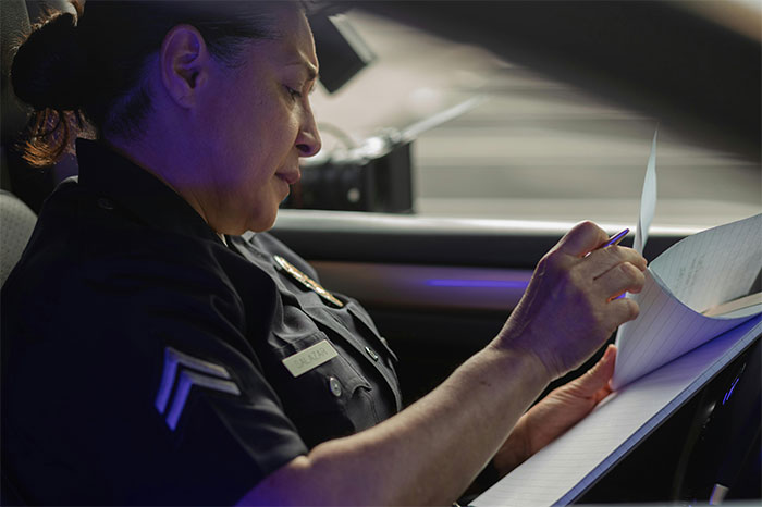 Police officer reviewing paperwork inside a patrol car, illustrating a moment of work failure or mistake.