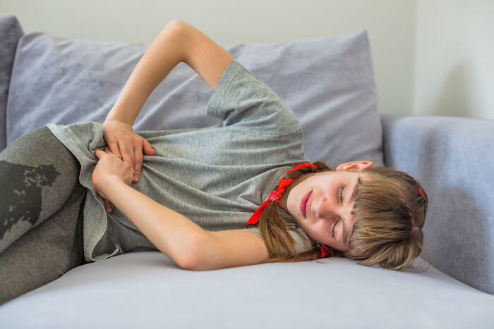 Young girl clutching her stomach on a couch, illustrating a worst Halloween experience turning fun into a nightmare.