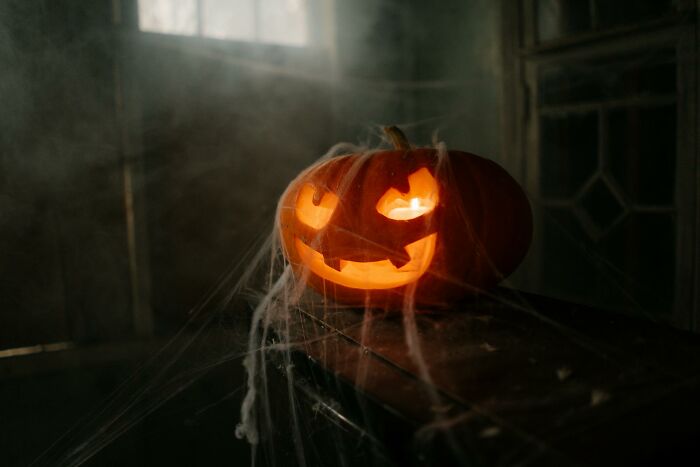 Glowing carved pumpkin with spider webs in a dark room, illustrating worst Halloween experiences turning fun into nightmare.