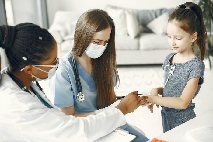 Two female doctors wearing masks examining a young girl's hand, highlighting worst Halloween experiences involving injuries.