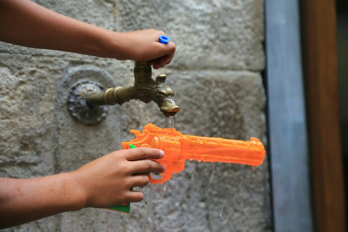 Child filling an orange toy gun with water from an outdoor Halloween water faucet during spooky activities.