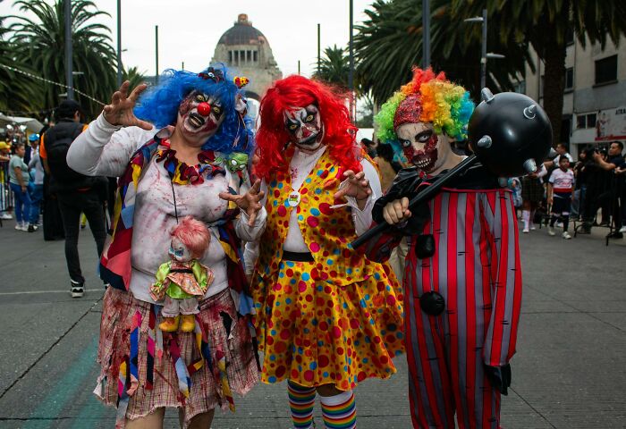 Three people in creepy clown costumes and makeup at a crowded Halloween event showing worst Halloween experiences.