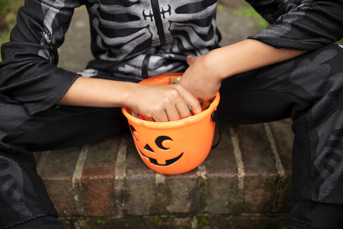 Child in skeleton costume sitting with pumpkin bucket, experiencing one of the worst Halloween moments turning fun into nightmare.