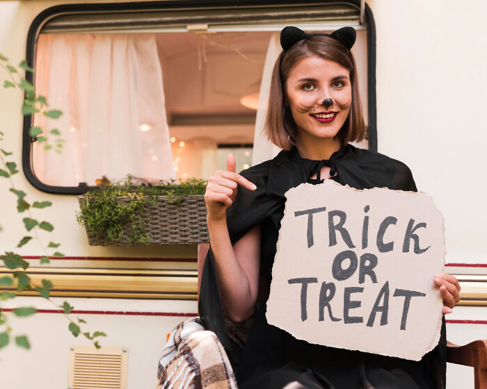 Young woman in a cat costume holding a trick or treat sign, illustrating Halloween experiences that turned into nightmares.