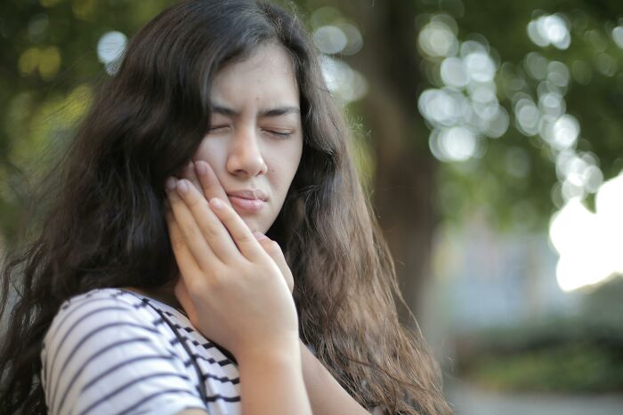 Young woman outdoors holding her jaw in pain, reflecting on mind-bending scenarios that challenge morals and decisions.