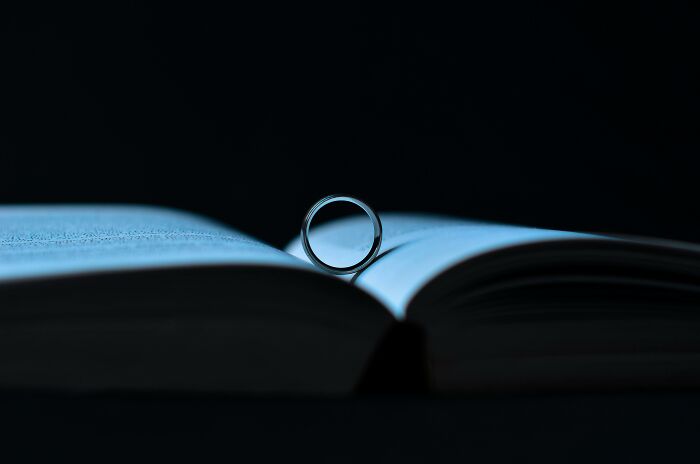 Silver ring standing upright on the pages of an open book in a low light setting, symbolizing mind-bending scenarios challenging morals.
