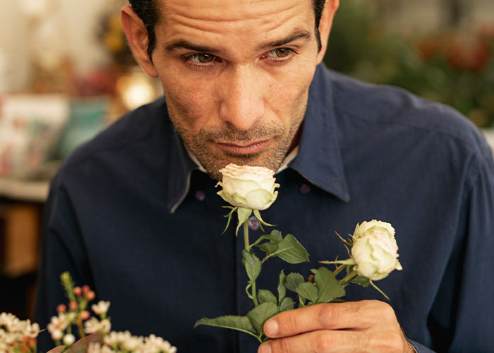 Man in a navy shirt smelling white roses, challenging common myths about men with a thoughtful expression.