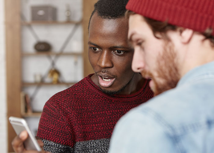 Two men sharing thoughts and reacting while looking at a smartphone, debunking common myths about men.