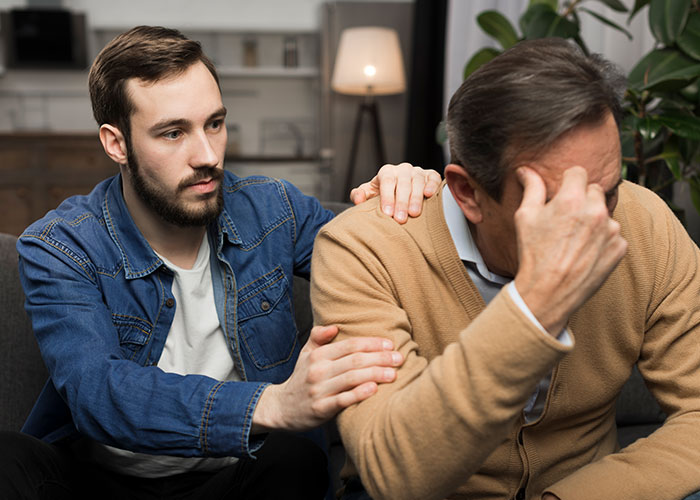 Young man comforting older man in a living room, illustrating common myths about men that are simply not true.