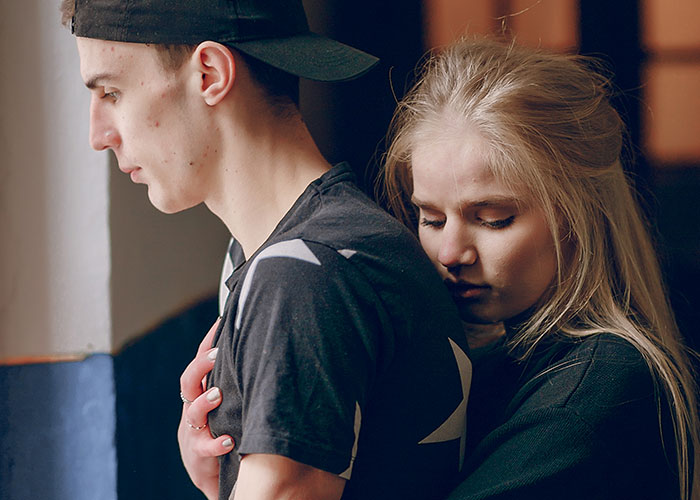A young woman hugging a young man from behind, illustrating emotional moments challenging myths about men.