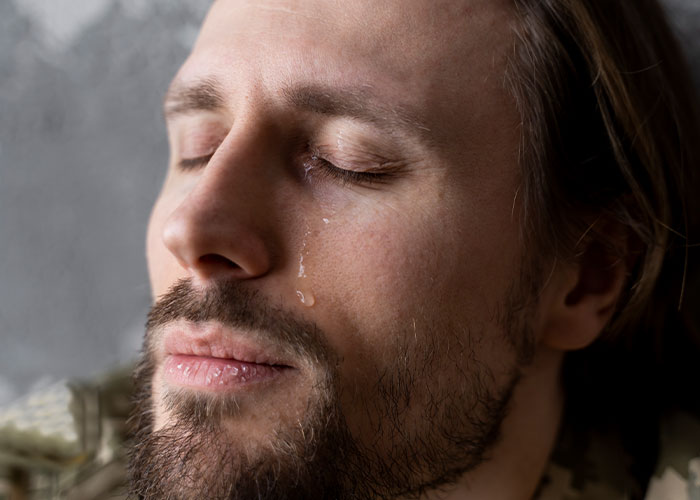Close-up of a man with closed eyes and a tear on his cheek, challenging common myths about men and emotions.