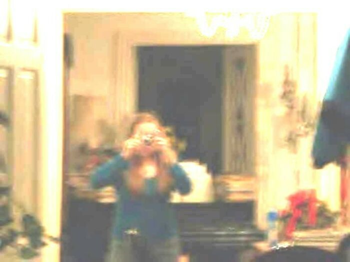 Blurry photo of a person taking a mirror selfie in a dimly lit room, creating a creepy and unsettling effect.