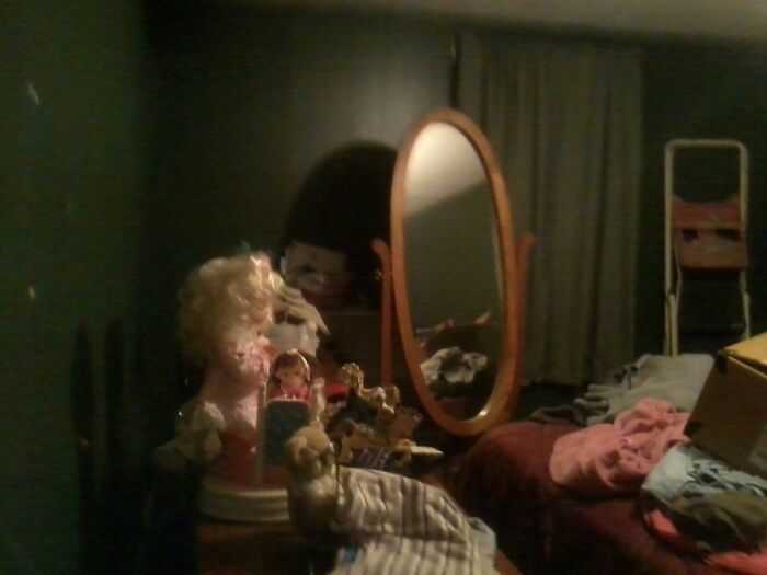 Dimly lit room with dolls and a mirror casting eerie reflections, a creepy photo that makes hearts skip a beat.