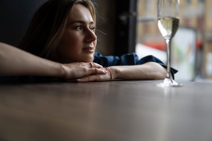 A woman sitting alone at a restaurant table looking thoughtful with a single glass of champagne nearby.