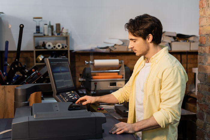 Young man using a digital printer in a workshop, exploring 24 loopholes to improve printing efficiency and results.