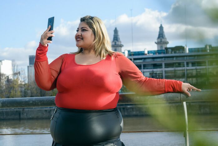 Woman in red top taking selfie outdoors near river, illustrating healthy habits and lifestyle concepts.