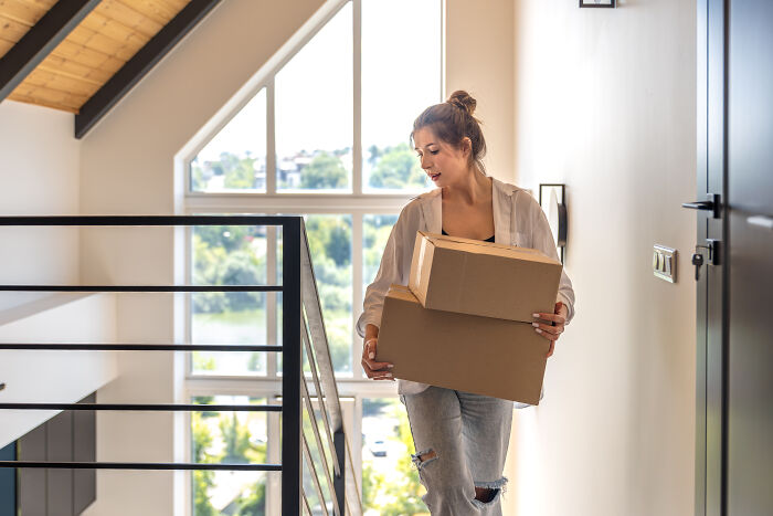 Young woman carrying cardboard boxes up stairs in a bright home, capturing everyday moments related to creepy experiences.