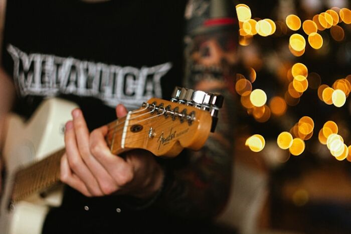 Close-up of a tattooed person playing Fender electric guitar, illustrating long grudges and personal expression through music.